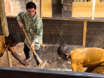 A young white man is holding a shovel, and two young black men in uniform are beside him, leaning towards the ground.