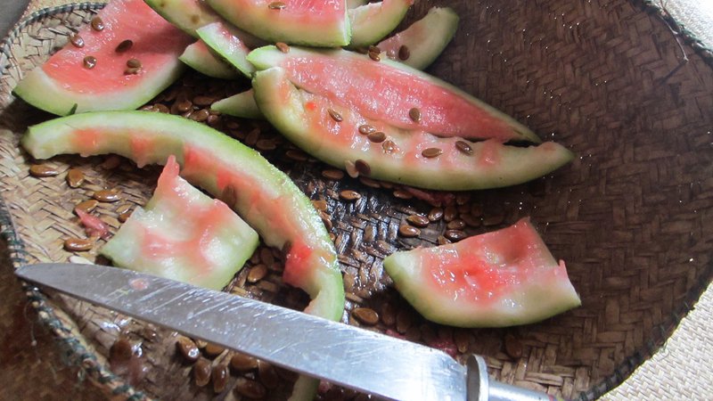 Watermelon rinds and seeds sit alongside a knife on a woven mat.