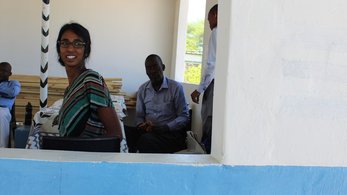 A Peace Corps Volunteer smiles from inside the window of a health clinic in Botswana. The walls are blue and white.