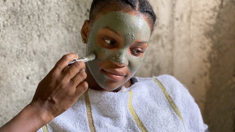 A girl covers another girl's face with a mud mask.