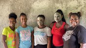 Five women stand together smiling. Two have mud masks on.