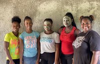 Five women stand together smiling. Two have mud masks on.