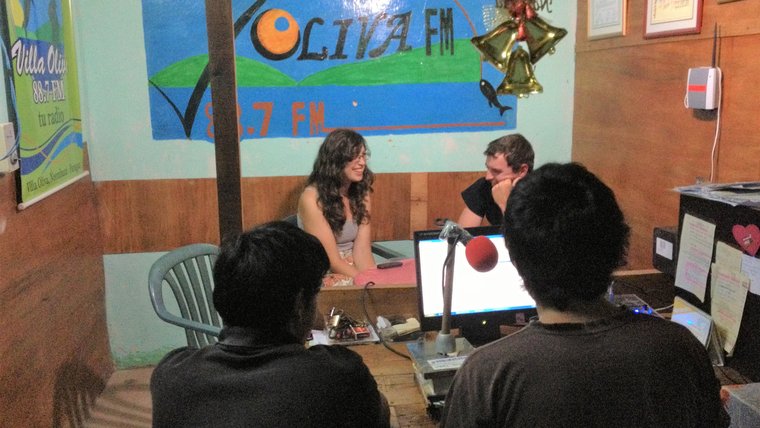 Three people from Paraguay and a white woman sit inside of a radio studio, doing interviews.