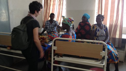 American friend of Volunteer greets Malawian women sitting on a bed in a health center