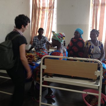 American friend of Volunteer greets Malawian women sitting on a bed in a health center
