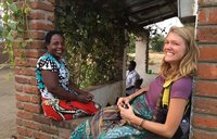 Volunteer Katlyn smiles at the camera while sitting on a brick porch with her smiling Malawian friend Katherine.