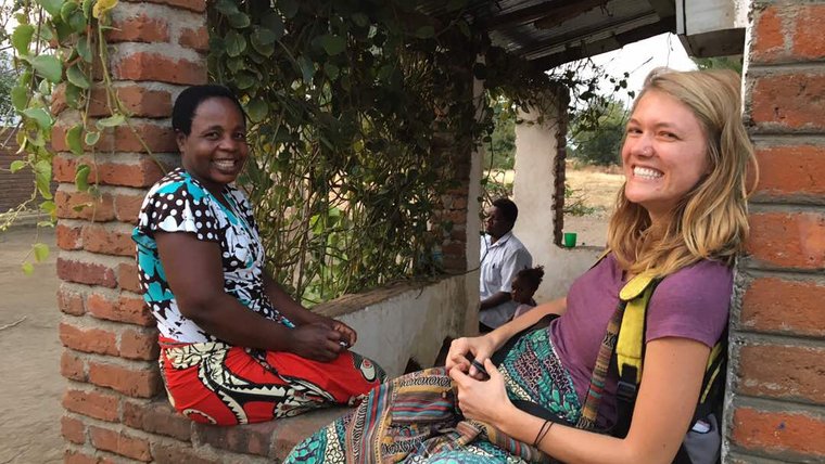Volunteer Katlyn smiles at the camera while sitting on a brick porch with her smiling Malawian friend Katherine.