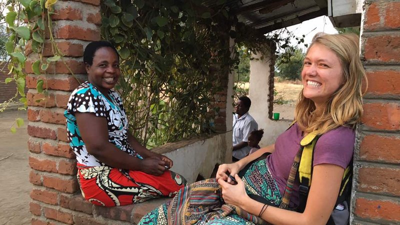 Volunteer Katlyn smiles at the camera while sitting on a brick porch with her smiling Malawian friend Katherine.