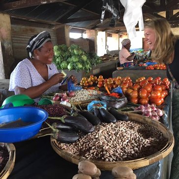 Volunteer Katlyn leans over a table of vegetables smiling to chat with a Malawian women selling them