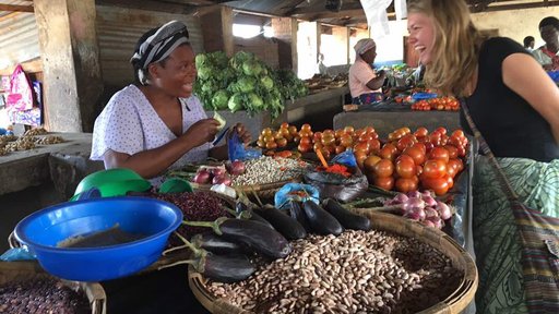 Volunteer Katlyn leans over a table of vegetables smiling to chat with a Malawian women selling them