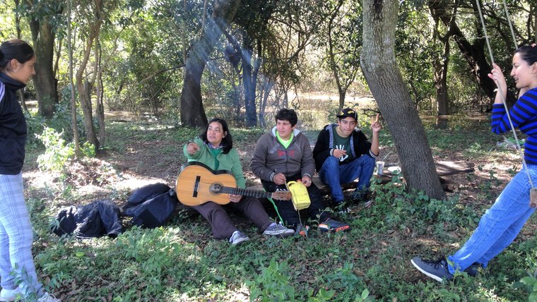 A group of three people sit under a tree with a guitar