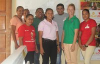 A female Volunteer stands smiling with her Guyanan coworkers inside of a health clinic.