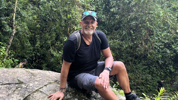 Man wearing a backpack is sitting on top of a rock surrounded by greenery.