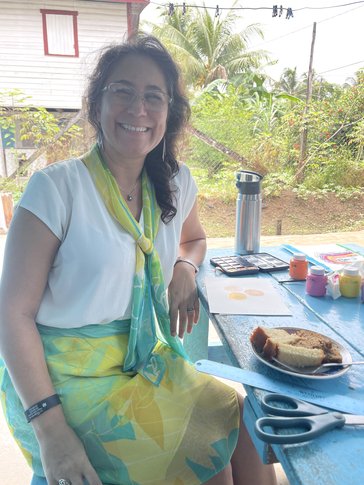 Volunteer sitting on bench with craft materials and a plate of cakes