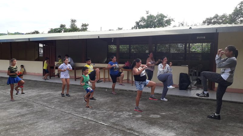 A black female teaches a group of Ecuadorian students how to kick box outside a classroom