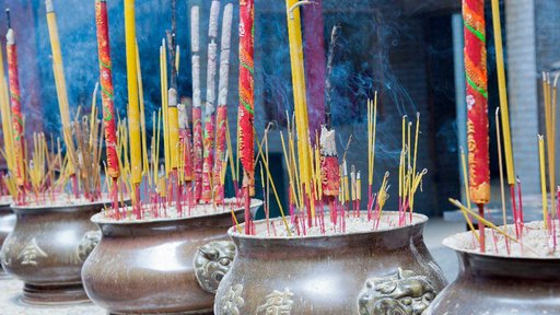 Pink, yellow, and red incense sticks stand upright in four urns at a temple.