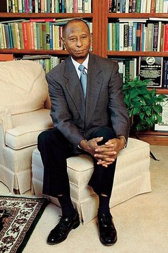 A older African American man in a suit sits in a home library.