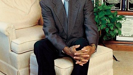 A older African American man in a suit sits in a home library.