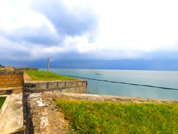 The weathered stone ramparts and grassy ruins of Mannar Fort overlooking the vast, calm waters of the Indian Ocean under an overcast sky