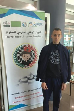 Ayman stands next to a large poster for a chess tournament