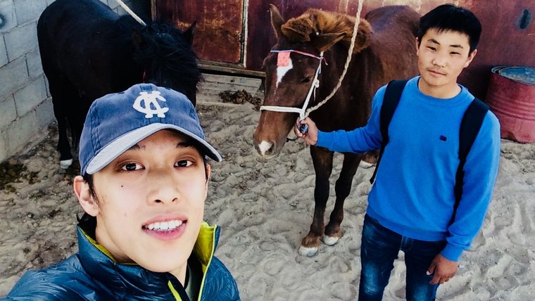 Two men take are taking a selfie. One is holding the reins of a brown pony.