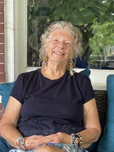 A woman sits on a patio smiling in a navy tee.