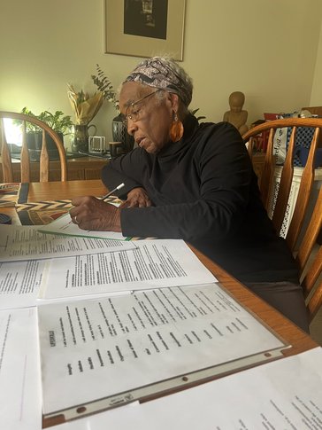 An older woman writes at her kitchen table