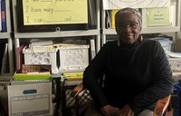 An older woman sits smiling in front of teaching materials