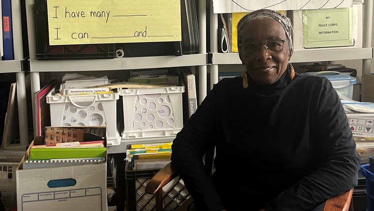 An older woman sits smiling in front of teaching materials