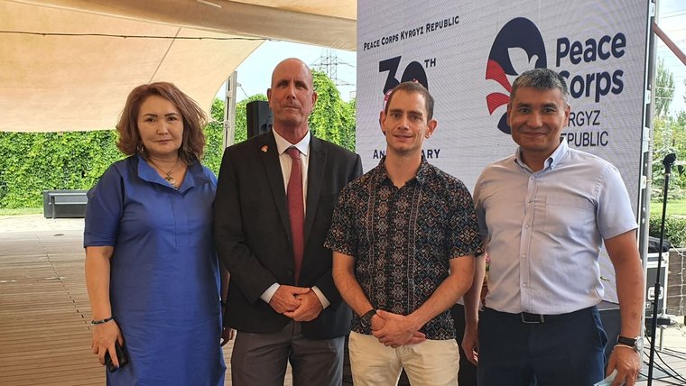 Three men and one woman stand in front of a Peace Corps sign