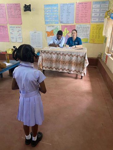 Kat and primary teacher, Ruben listen to a student’s oral performance.