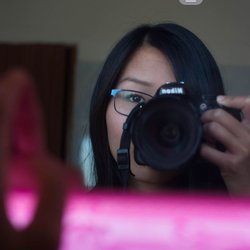An Asian-american female looksat a mirror through the lens of a DSLR camera