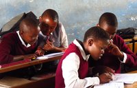 School kids dressed in uniforms reading at their desks.