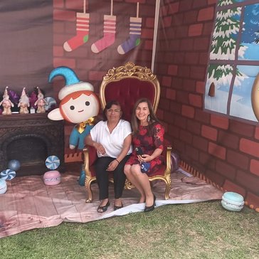 Two women sit in a red velvet chair with Christmas decorations around them.