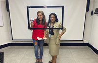 Two women stand behind a suspended, black frame.