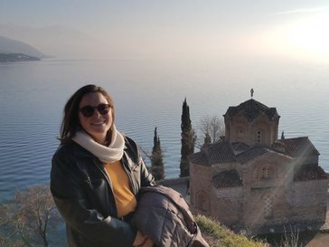 A woman in sunglasses smiles in front of an ocean view