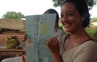 A female Volunteer sits outside and hold up a drawing of nutritious foods and moringa