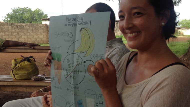 A female Volunteer sits outside and hold up a drawing of nutritious foods and moringa