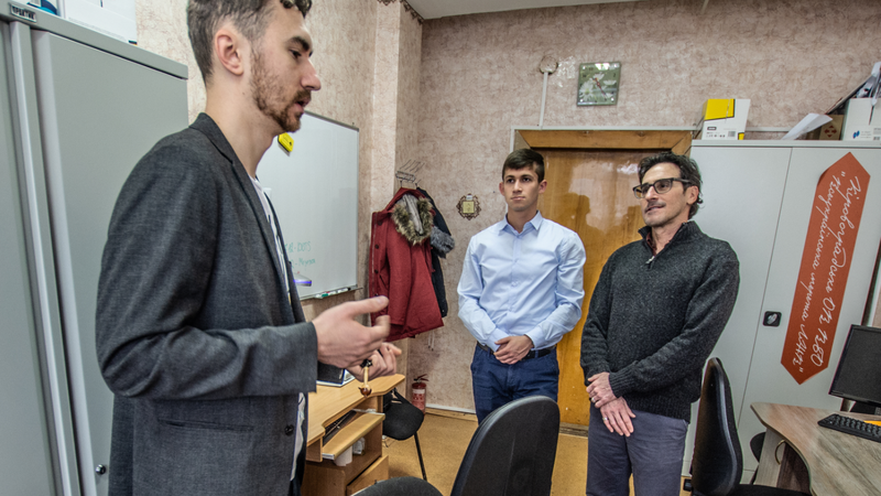 A young Ukrainian man stands speaking to two other men. He is dressed in a blazer.