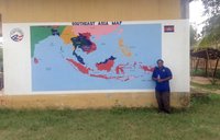 A man in a blue Peace Corps shirt stands beside a painted Southeast Asia map