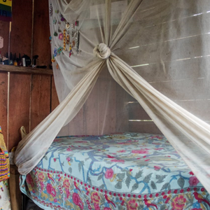 A bed with a mosquito net tied up inside of a wooden house