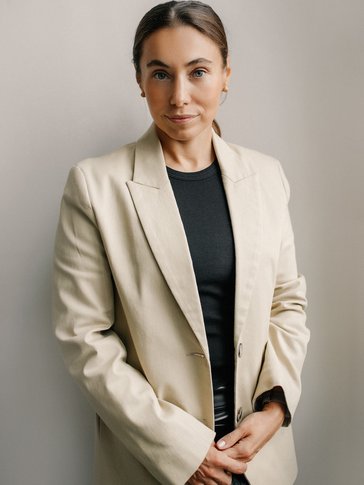 A woman stands in a beige blazer
