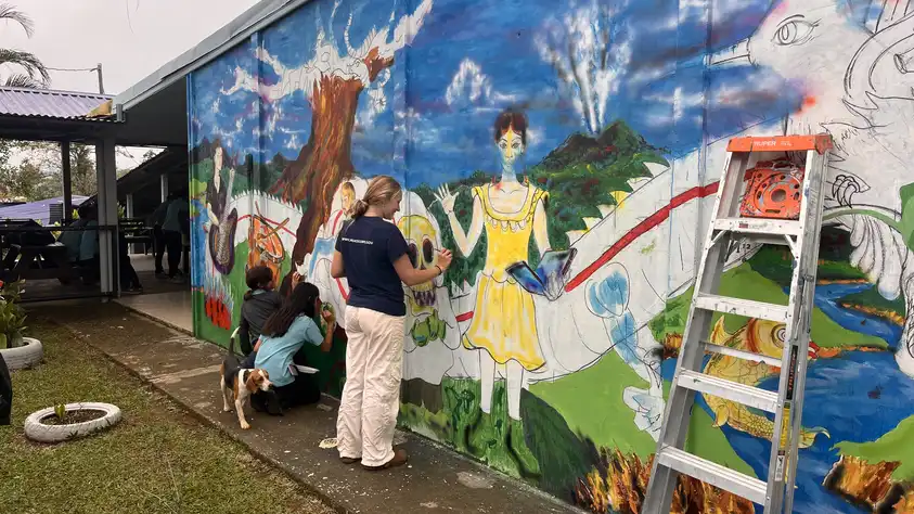 Phoebe paints a mural at the entrance of the high school with students.