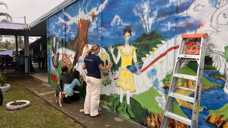 Phoebe paints a mural at the entrance of the high school with students.