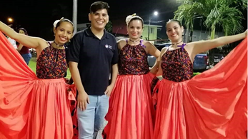 A male peace corps volunteers stands with 3 female dancers wearing bright pink skirts