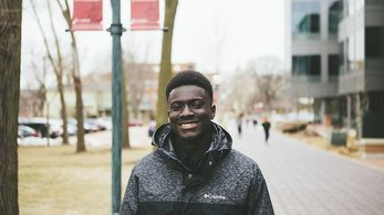 A Ghanaian twenty-something male smiles outside on a city street.