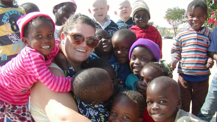 A female Volunteer joins a group hug with lots of her students.