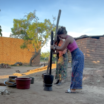 Neighbors teach Sophie how to grind groundnuts for cooking.