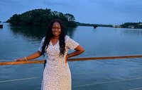 A woman stands in a patterned dress in front of the ocean