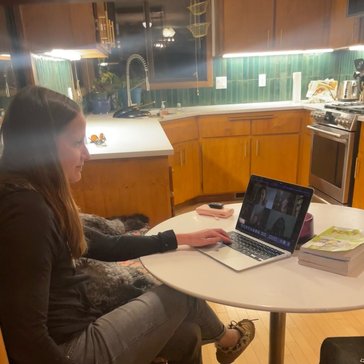 A woman joins a virtual meeting with her poodle dog beside her